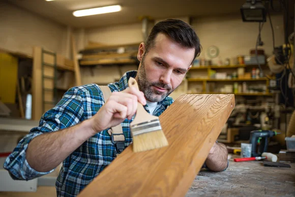 Person streicht Holz mit Pinsel